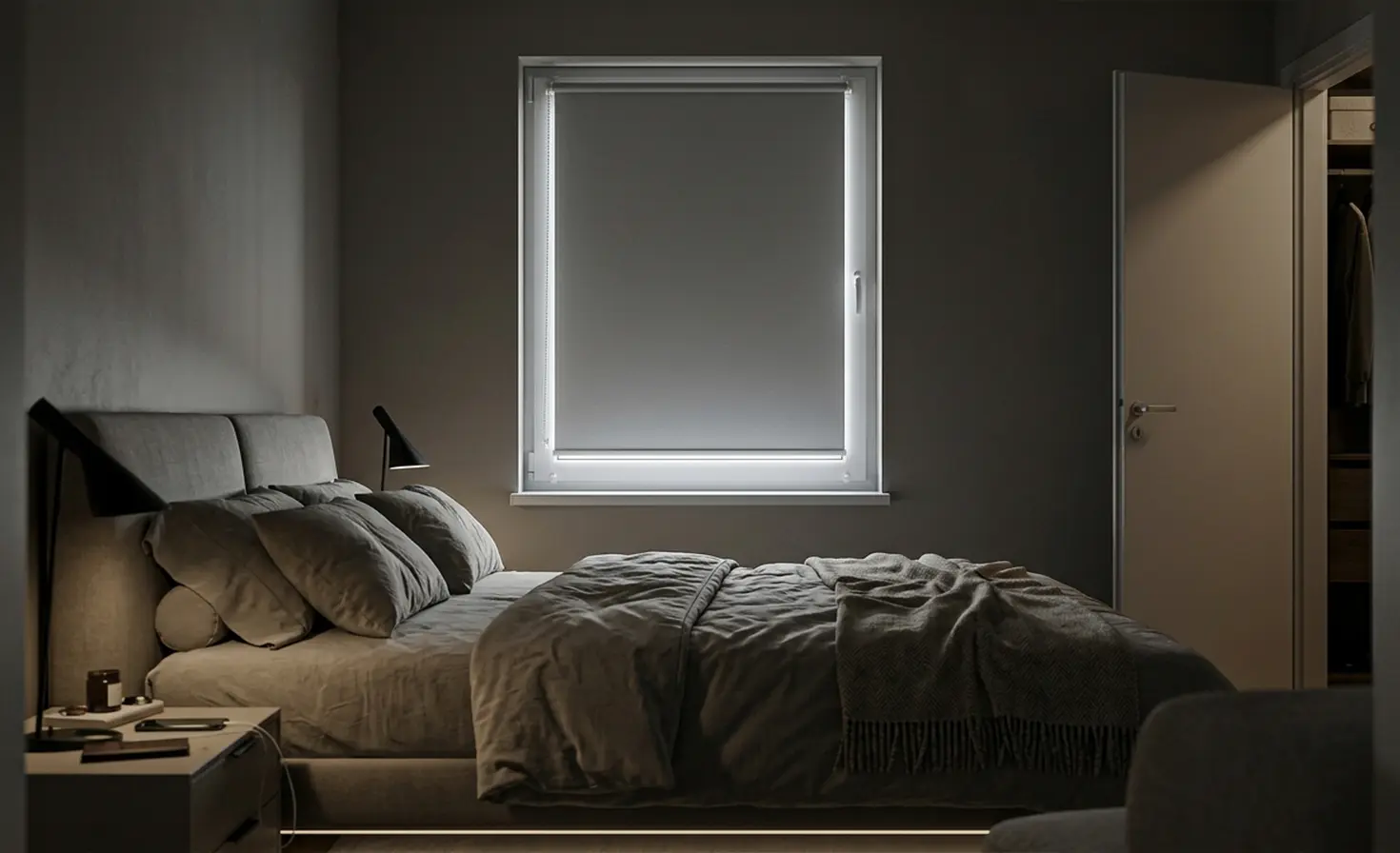 Dark bedroom in the morning with a grey blackout roller blind on the window